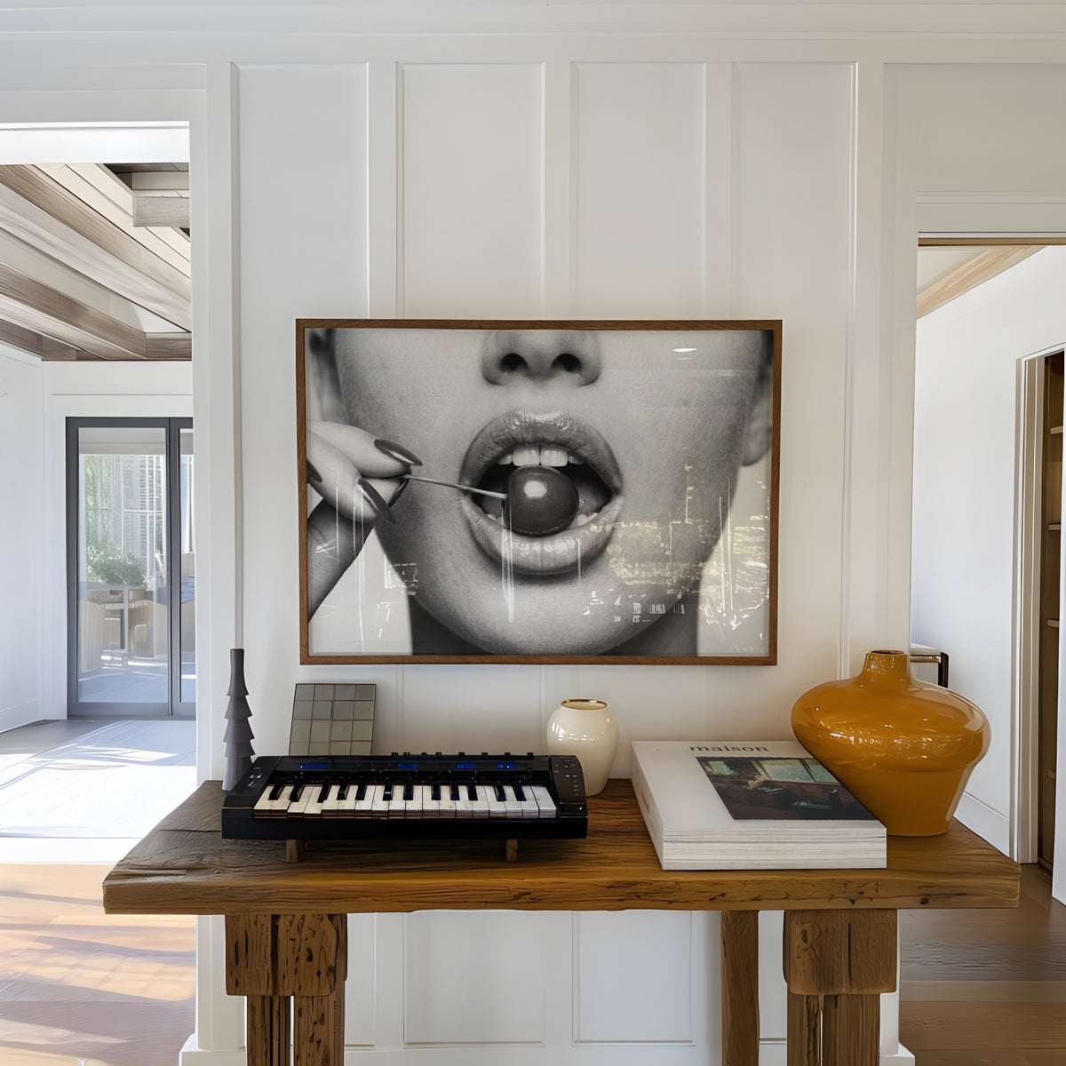 A framed black and white art print "cherry bomb" depicting a close-up of a person's mouth holding a cherry, hanging above keyboard on a wooden table