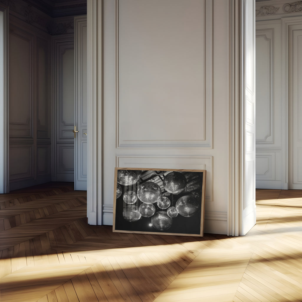 Framed monochromatic disco party artwork on a wooden floor with sunlight streaming through a window.