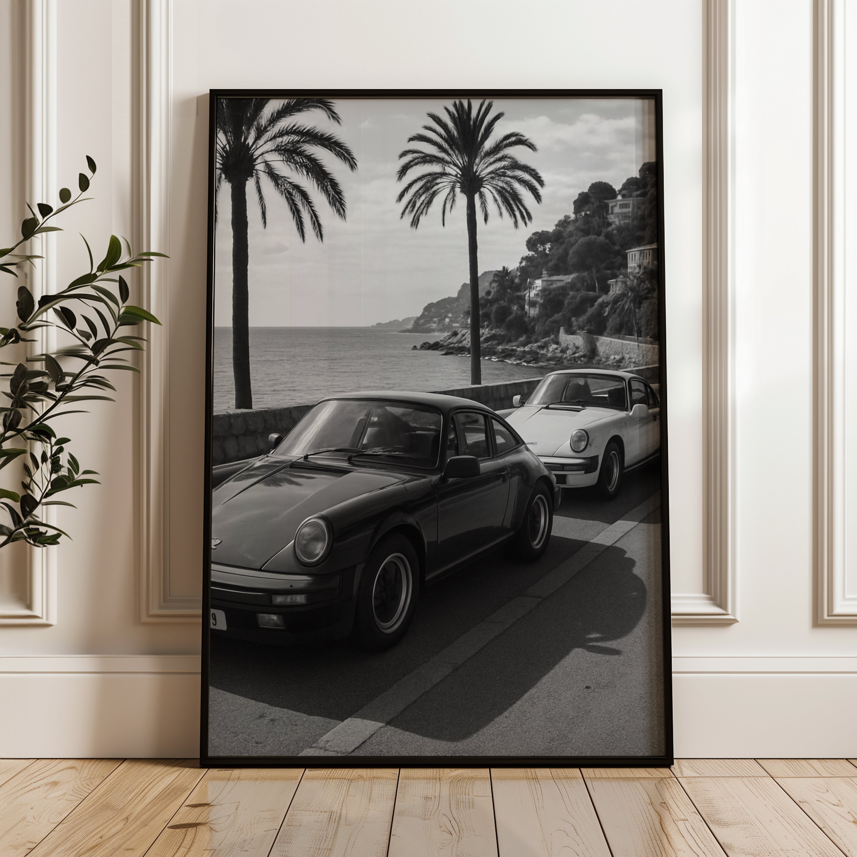 Framed French Riviera black and white print of vintage cars by a coastal road with palm trees.