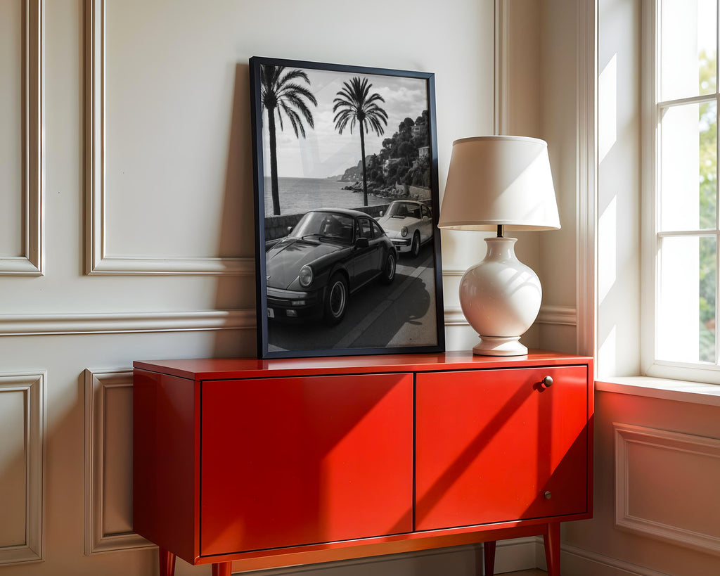 Red cabinet with a lamp and framed French Riveria poster  in a room with a window.