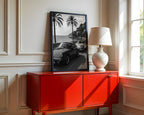 Red cabinet with a lamp and framed French Riveria poster  in a room with a window.