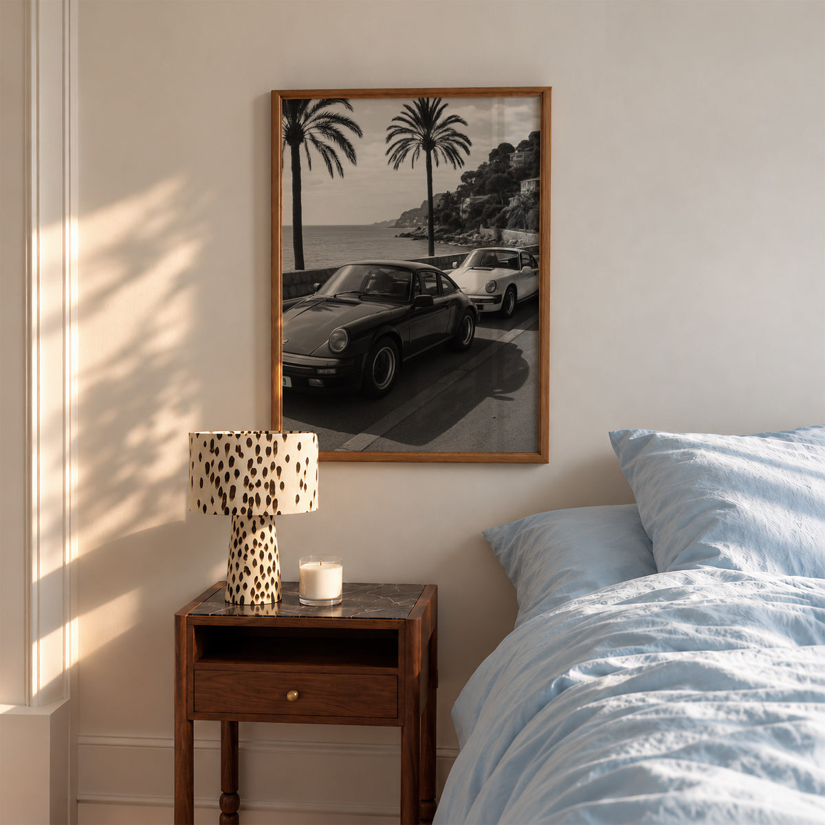 framed black and white French Riviera poster print hanging above nightstand in bedroom