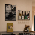 framed black and white French Riviera poster print hanging in kitchen next to wine rack and cook book