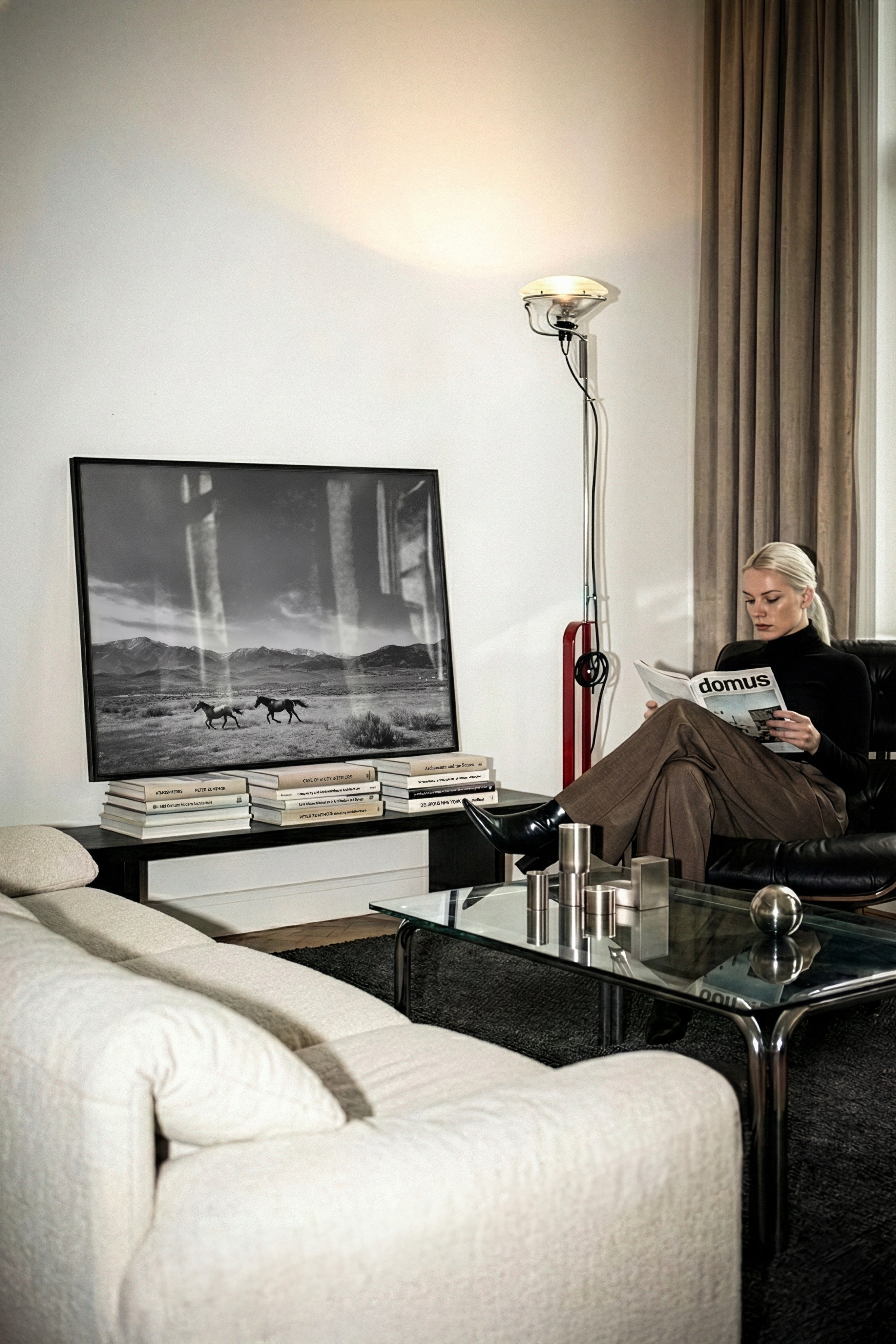 framed black and white wall art sitting on stack of coffee table books leaning against wall in living room with chic woman reading a magazine