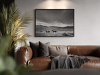 black and white wester wall art frame hanging above brown leather couch next to palm tree in living room