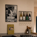 framed champagne showers black and white poster print hanging in kitchen next to wine rack above cook book