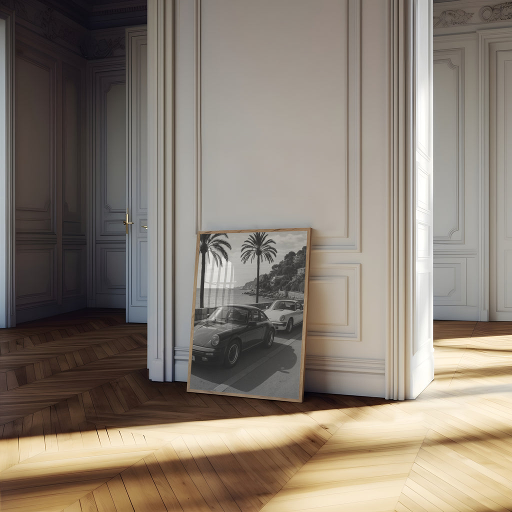 Framed French Rivera black and white artwork leaning against a wall in a sunlit room with wooden floors.