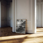 Framed French Rivera black and white artwork leaning against a wall in a sunlit room with wooden floors.