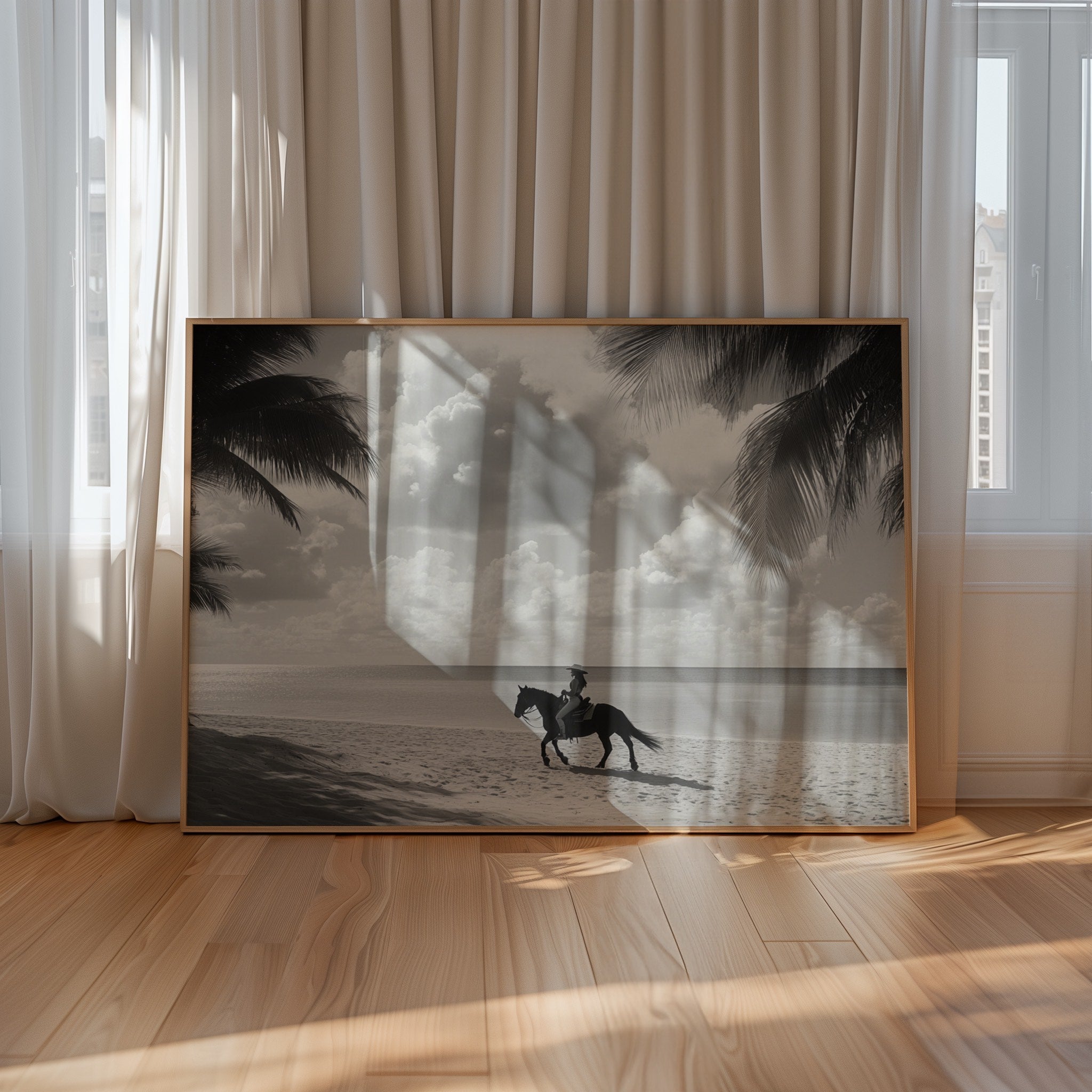 Framed artwork of a person riding a horse on a beach with palm trees, displayed in a room with curtains and wooden floor.