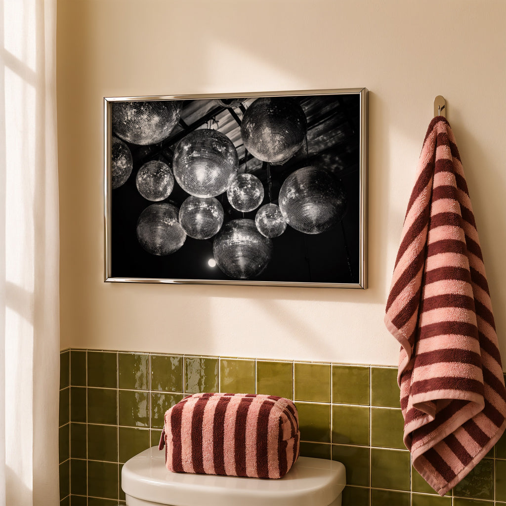 framed black and white disco ball poster print hanging above toilet in bathroom with green wall tiles 