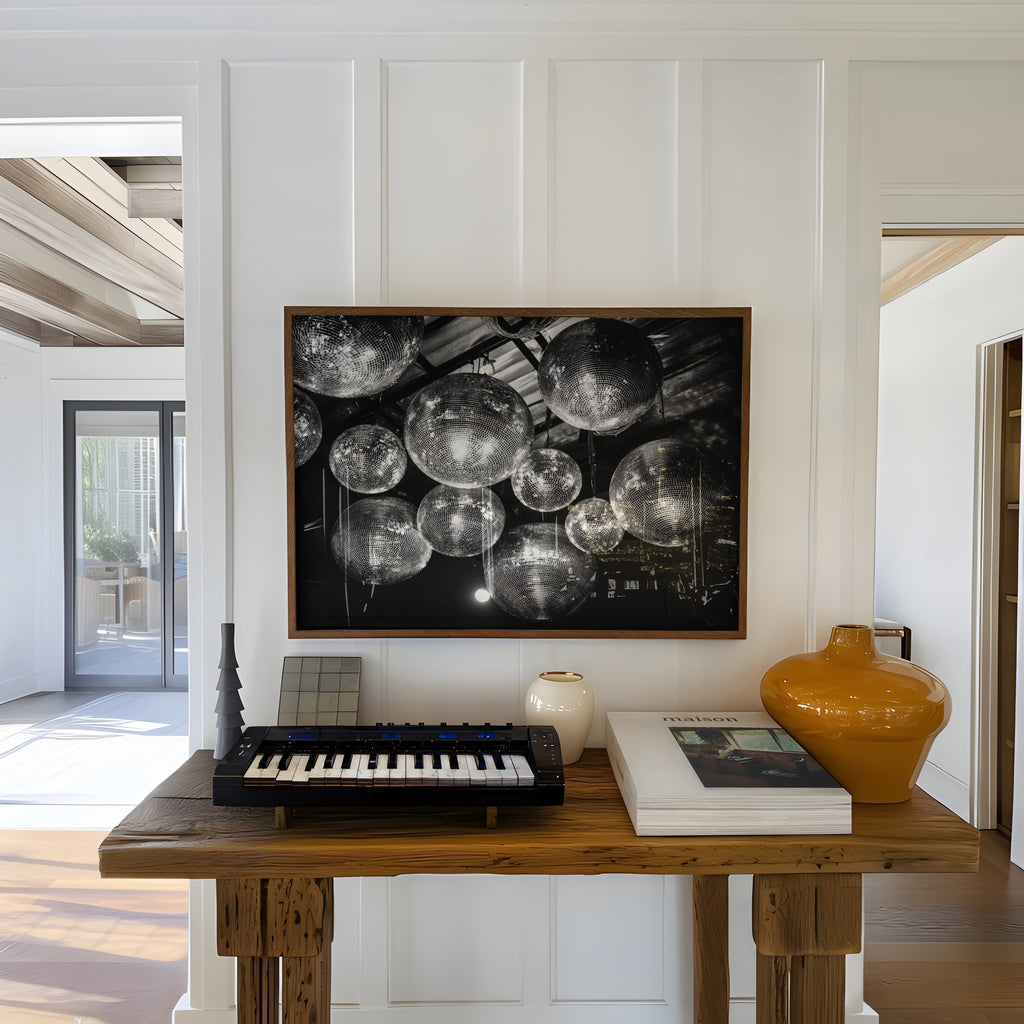 Wooden table with keyboard, books, and vases against a white paneled wall with a large framed black and white disco party print 