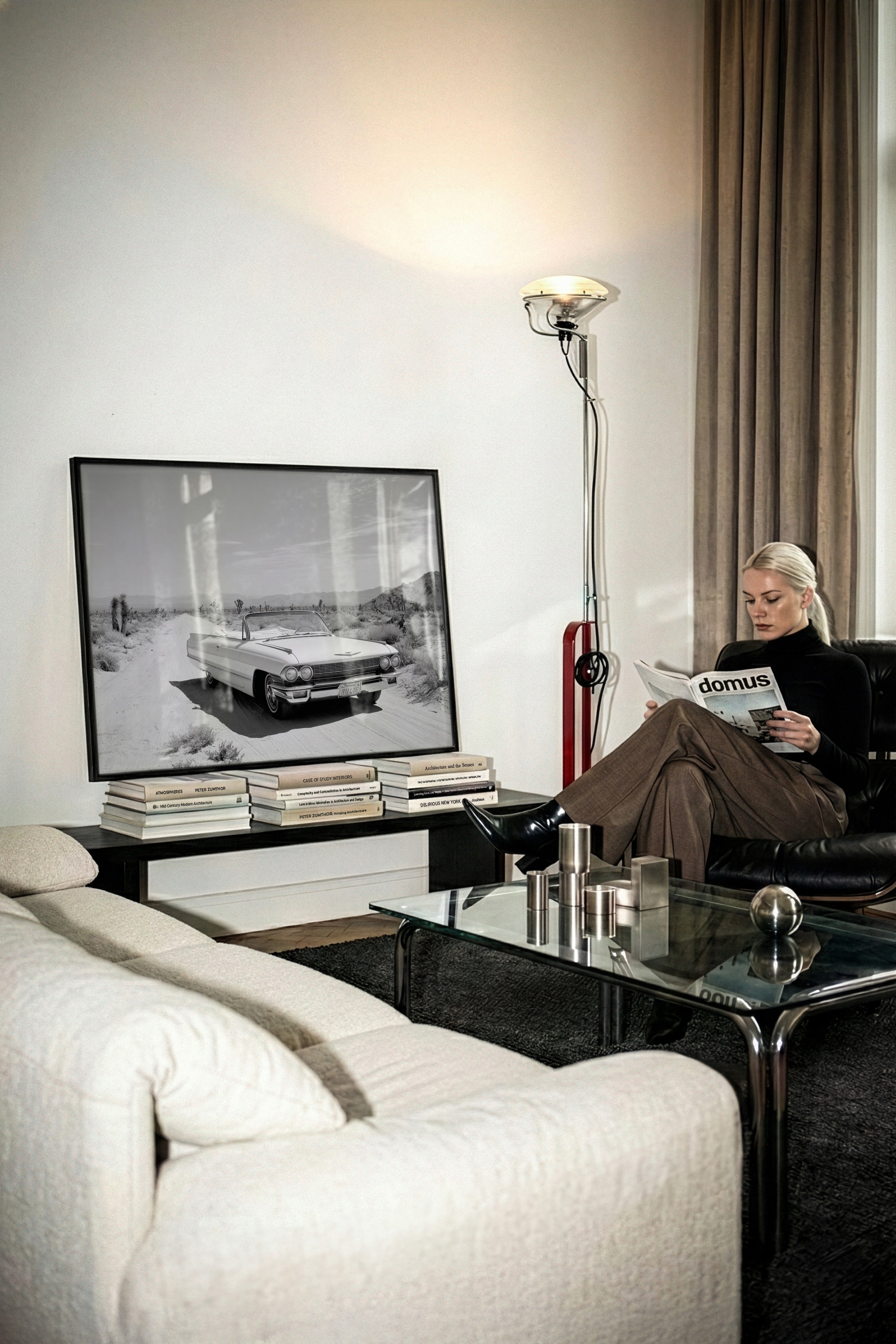 Modern living room with a woman reading a magazine, a coffee table with books and a lamp, and a Framed black and white dust and dreams wall art  print on the wall