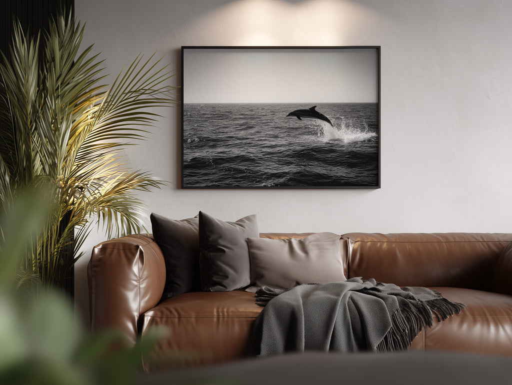 framed black and white flipper poster print hanging above brown leather couch next to palm tree