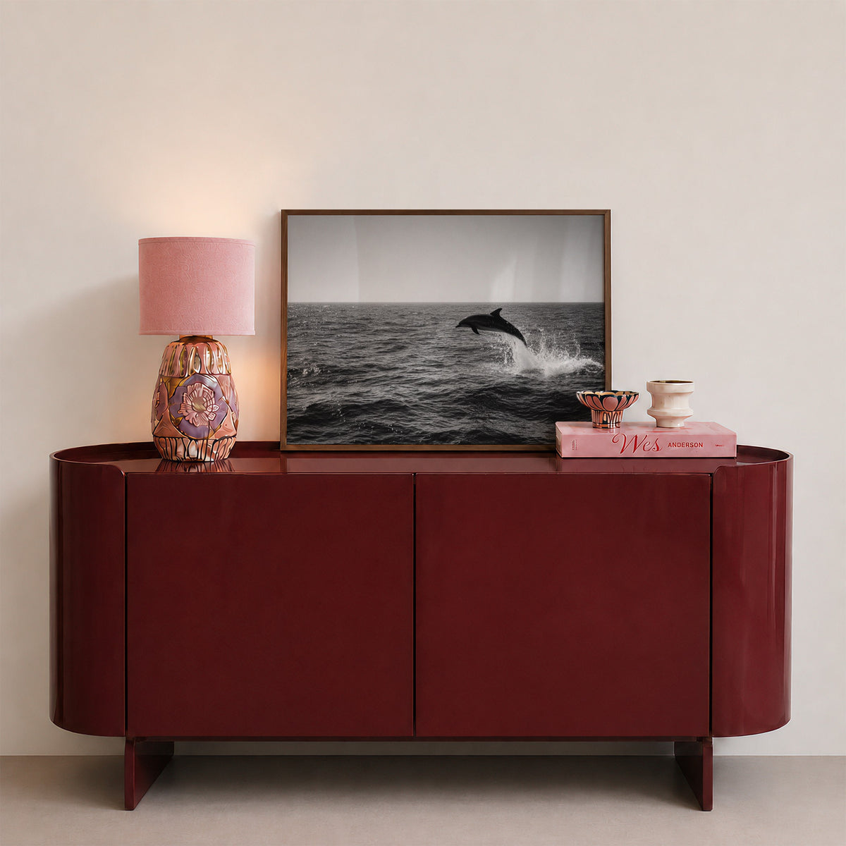 framed black and white dolphin print sitting on red console in entryway with pink decor