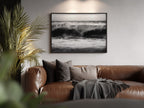 Brown leather sofa with cushions and a blanket in a living room setting, featuring a framed black and white high tide poster print  on the wall.