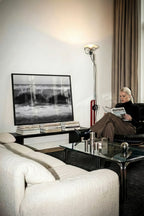 Modern living room with a woman reading a magazine, a large TV, and stylish decor.   framed black and white high tide poster print sitting on coffee table books leaning against the wall