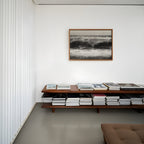 Wooden shelf with books and a fframed black and white high tide poster print wall art on a white wall.