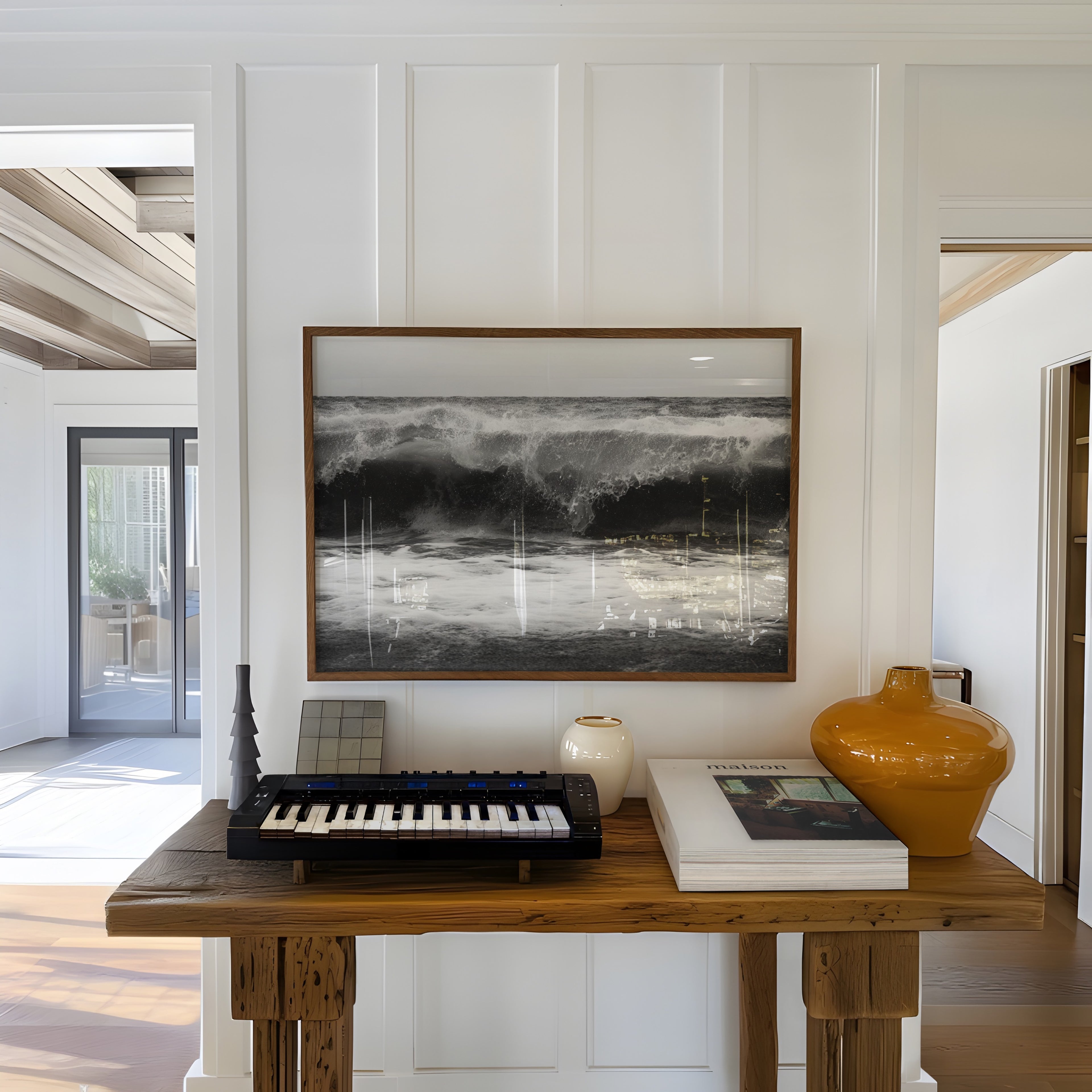 Music keyboard on a wooden table with a framed black and white high tide poster print above, in a bright room.