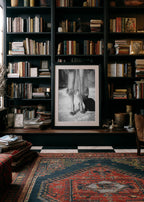 old money library Bookshelf with books and a framed black and white kitty kitty poster print in a room with a patterned rug.