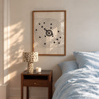A framed moving target wall art print featuring a black bullseye with a heart at the center hanging in bedroom over nightstand