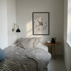 A framed moving target wall art print featuring a black bullseye with a heart at the center hanging above the bed in a bedroom