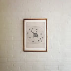 A framed moving target wall art print featuring a black bullseye with a heart at the center, hanging on a white painted brick wall.