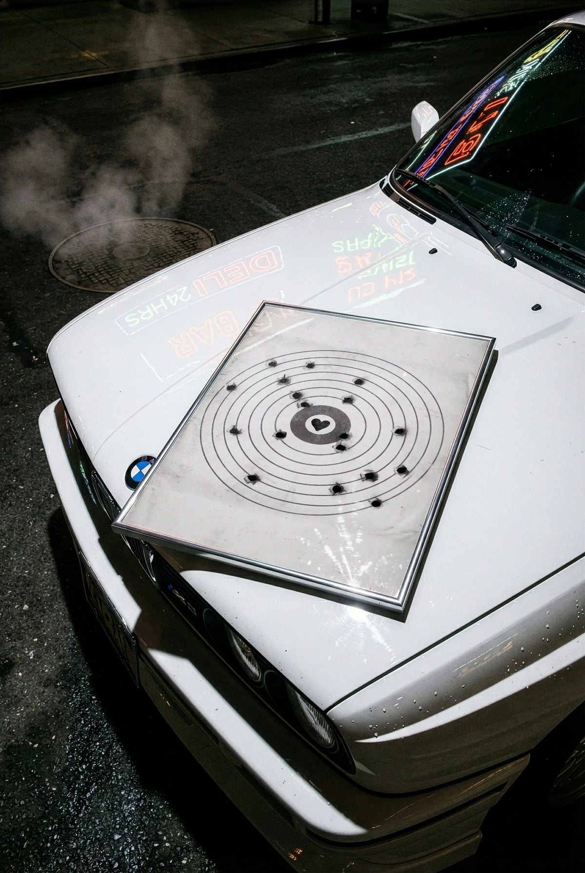 A framed moving target wall art print featuring a black bullseye with a heart at the center sitting on the hood of a BMW car