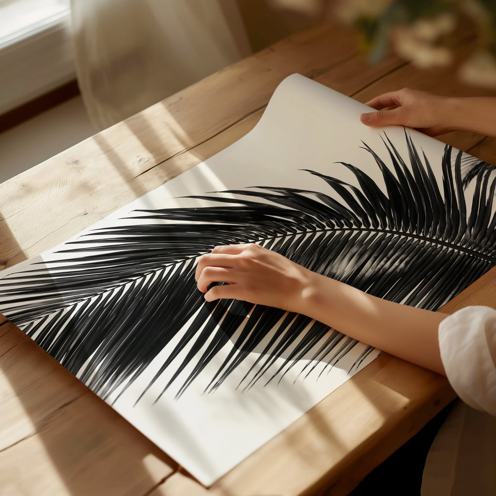 two hands holding black and white paradise palm poster print on a wooden table