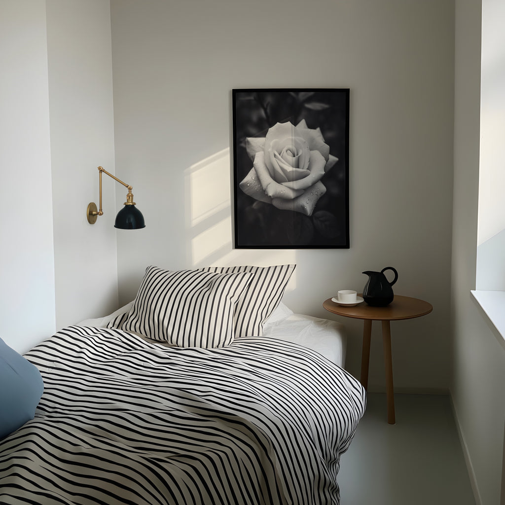 Bedroom with striped bedding, a side table with a pitcher, and a framed black and white rose on the wall.