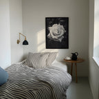 Bedroom with striped bedding, a side table with a pitcher, and a framed black and white rose on the wall.