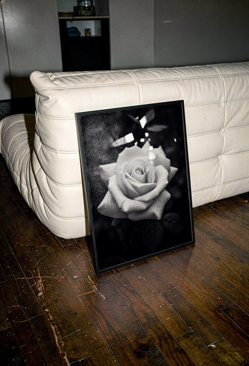Framed black and white rose art print on a wooden floor with a white couch in the background