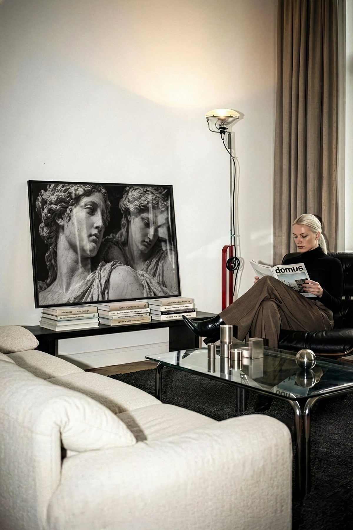 black and white set in stone roman statue poster print wall art sitting on stack of magazines leaning against the wall while a chic woman sets next to it reading