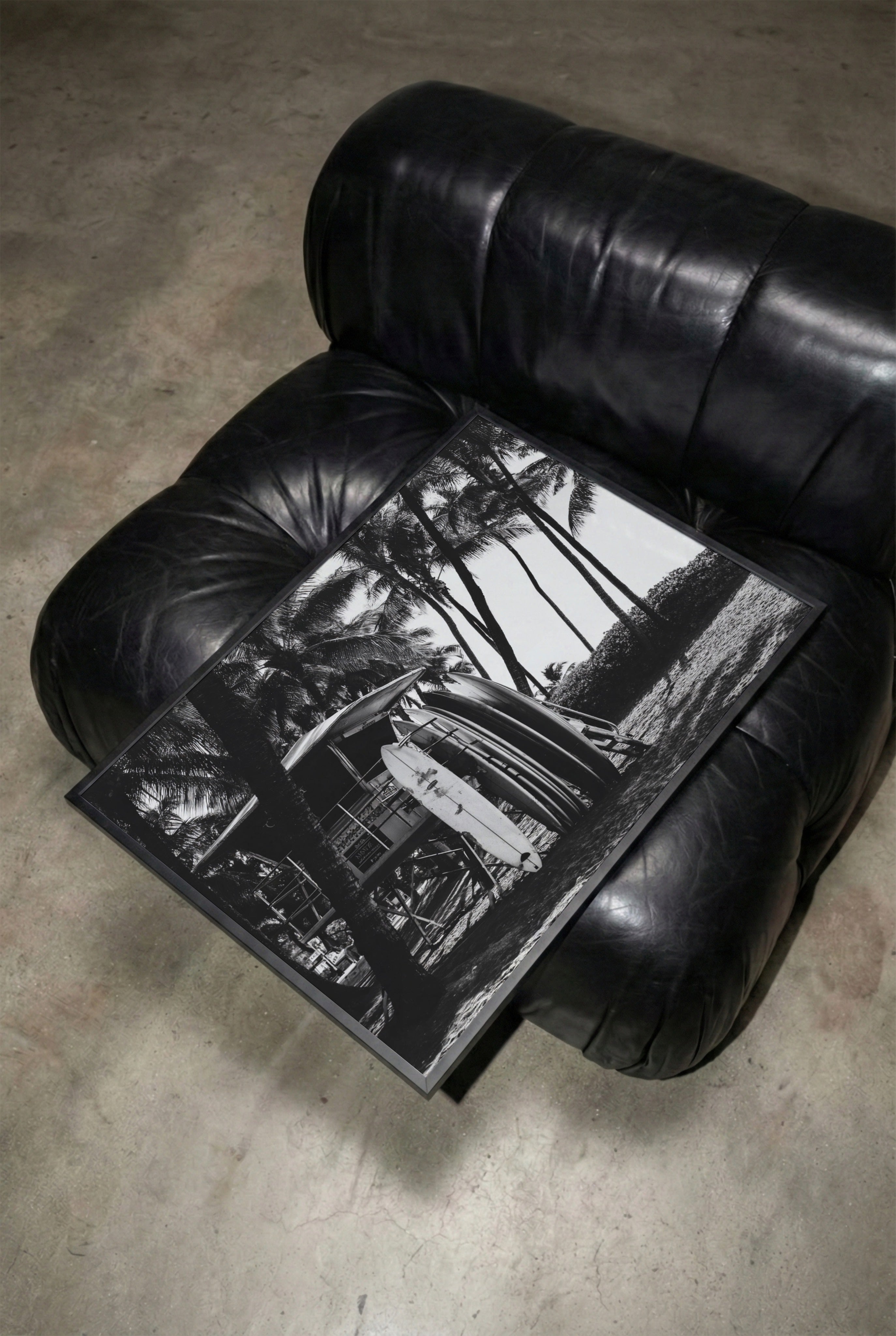 Black leather armchair with a Framed black and white Surfs Up poster print  on a concrete floor.
