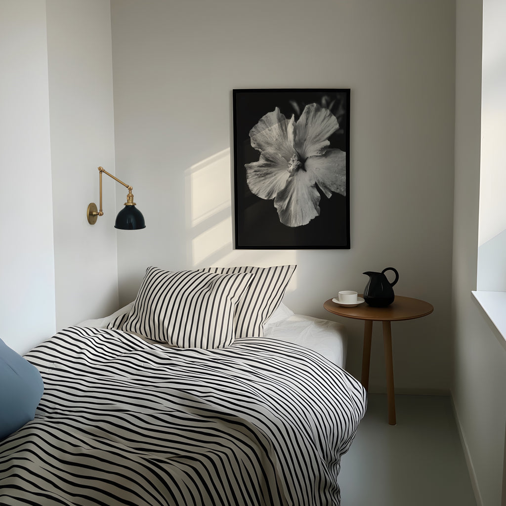 Modern bedroom with striped bedding, side table, and framed black and white tropical bloom floral wall art print above bed. 